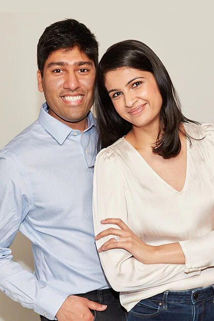 Portrait of a smiling man and woman standing together, with the man in a blue shirt and the woman in a cream blouse.